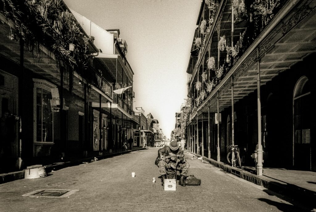 Black-and-white photo of a street musician in New Orleans' French Quarter, showcasing historic architecture.